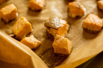 Close-up of raw fresh salmon fillets cut into cubes and arranged on parchment paper in a tray, ready for cooking, showcasing their quality and freshness