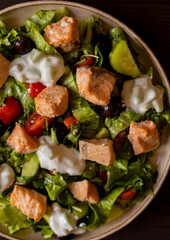 Close-up of a delicious Mediterranean salad featuring pieces of salmon fillet and a dollop of tzatziki sauce, offering a fresh and flavorful dining experience