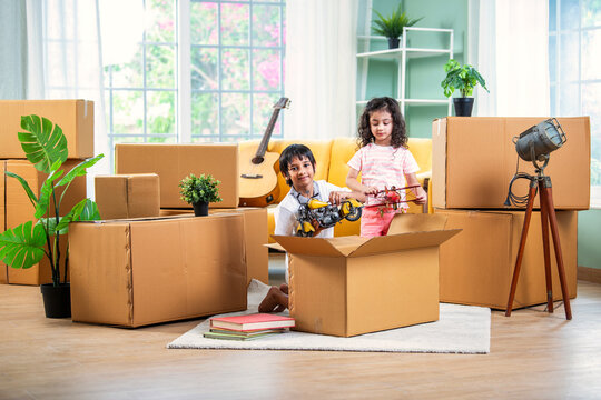 Indian siblings or kids playing or opening cardboard cartons on shifting or moving day