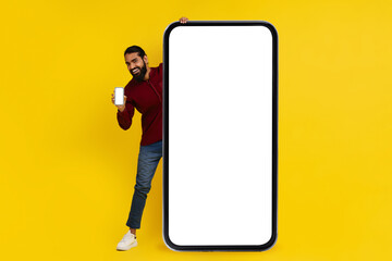 Positive indian guy standing by big phone with white screen
