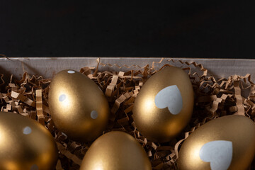 Close-up view of Gold eggs in paper box on black background.