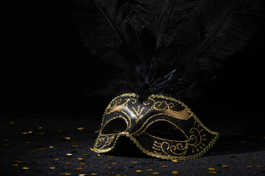 Masquerade gold mask with feathers and confetties on black background..