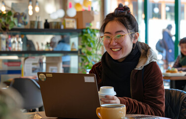 A focused woman sits in a cozy cafe, sipping coffee while engaging with work on her laptop, capturing everyday productivity