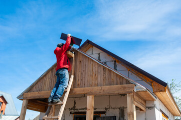 A worker builds a roof in a house while standing on a wooden ladder. Blue sky - 762422801