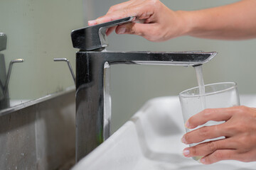 Woman filling glass with tap water from basin