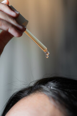 The girl puts on her black hair of hydrolyte from a pipette hair tonic