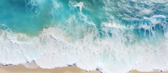 A majestic aerial view of azure waves crashing onto the sandy beach, forming foamy white peaks under a cumulusfilled sky with a gentle breeze - obrazy, fototapety, plakaty
