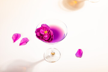 Cold purple violet exotic cocktail in glass with decorated flowers and petals.
