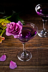 Cold purple violet exotic cocktail in glass with decorated flowers and petals. Tropical vibes.