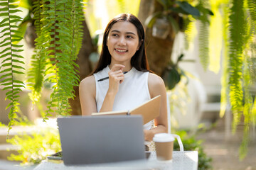 Asian woman looks for inspiration and comes up with project ideas while working on her laptop in a...