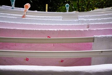 Pinke und weiße Bettwäsche auf weißem Wäscheständer mit Wäscheklammern zum Trocknen im Garten...