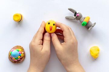 The hands of a small child are holding a yellow plasticine chicken.