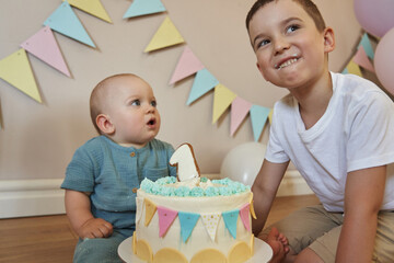 A little boy celebrates his first birthday with a cake topped with a number one, while his brother...
