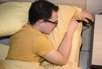 Young man with black eyeglasses sleeping turned in bed.