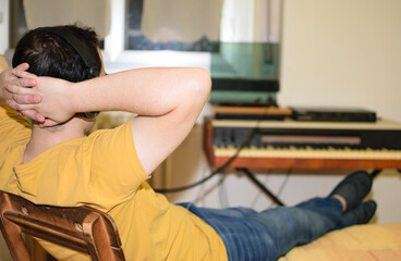 Young man relaxed with arms on back of his neck listening music with headphones