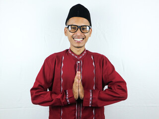 Asian Muslim man wearing glasses smiling to give greeting during Ramadan and Eid Al Fitr celebration over white background