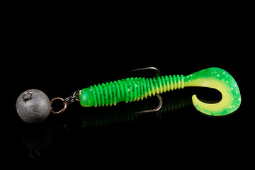 Soft fishing bait, green plastic grub, with double hook and lead sinker, isolated on black