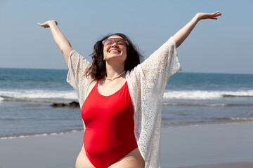 A girl with a lush sizes plus size in a red swimsuit is resting on a sandy beach against the ocean or sea