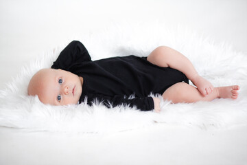 Ilittle baby dressed in a faithful bodysuit is lying on a white plush blunket