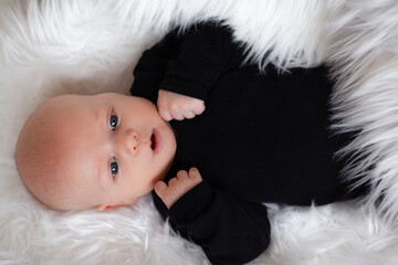 Ilittle baby dressed in a faithful bodysuit is lying on a white plush blunket