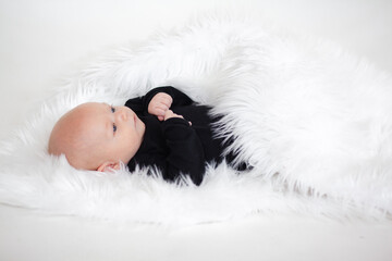 Ilittle baby dressed in a faithful bodysuit is lying on a white plush blunket