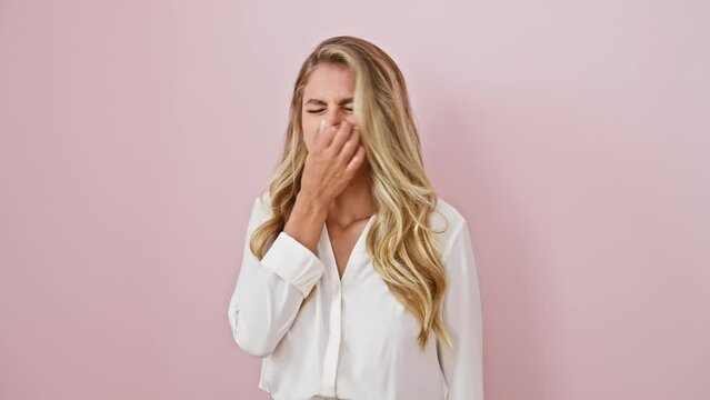 Young blonde woman in shirt, standing in disgust over isolated pink background, holds breath and nose at stinky bad smell, revealing a strong stench intolerance from an unpleasant surprise.