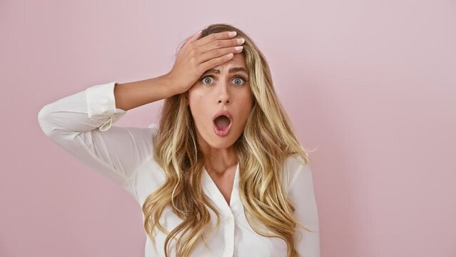 Astonished young woman, blonde and vibrant, wearing a shirt, standing shocked over a pink isolated background. expressive face of fear, amazed disbelief, shocked wonder, and excited surprise