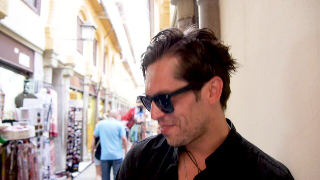 Very funny handsome man in black shirt and sunglasses greets camera with victory signs at Granada market