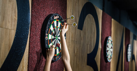 A dartboard is mounted on the wall, surrounded by plastic darts that have been carelessly thrown,...