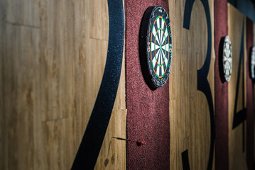  The wall features a dartboard with plastic darts scattered around it, none of which have hit the...