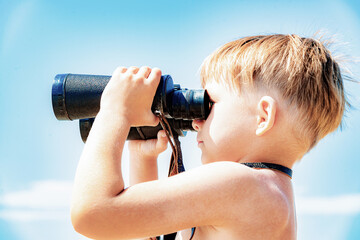 A boy with binoculars looks at the sea against a blue sky.