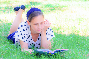 A girl lies on the grass under a tree and reads a book.