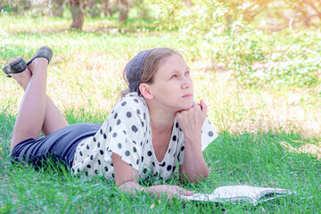 A girl lies on the grass under a tree and reads a book.