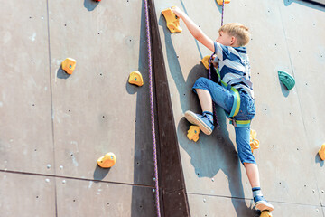 A boy in climbing equipment conquers the top of an artificial tower for climbers in a sports extreme recreation park. - obrazy, fototapety, plakaty