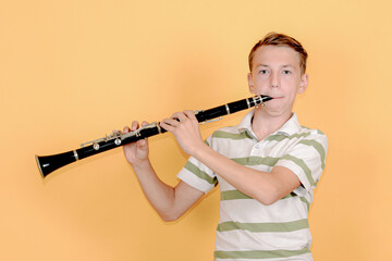 Boy musician playing the clarinet on a yellow background.
