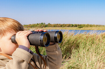 A boy with binoculars in the reeds is watching the wildlife.