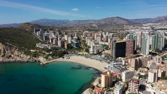 Aerial drone footage of the town of Benidorm in Spain in the summer time showing the beach known locally as Playa de Finestrat and hotels and apartments around the small beach