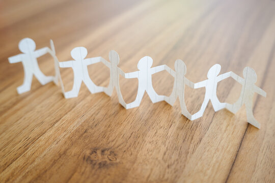 White paper human chain standind on brown wood background, teamwork concept