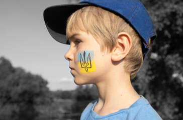 boy with national symbol painted on his cheek - trident on blue yellow background. Ukrainian...