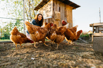 Joyful woman in chicken coop enjoying farm life by feeding chickens. Smiling farmer caring for her bird in her backyard in a rustic style, demonstrating an eco-friendly lifestyle