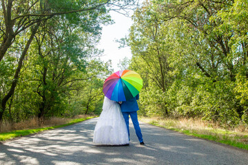 The bride and groom with a multi-colored umbrella stand on the background of the road	
 - Powered by Adobe