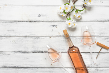Rose wine in a bottle and glasses, a corkscrew and a decorative cherry branch on a white wooden table. Top view, flat lay, copy space. Spring wine tasting concept. - 762495652