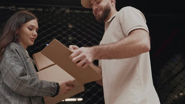 A friendly delivery man is giving a parcel to a young woman. Both individuals are engaged in a positive interaction, likely signifying a successful delivery service encounter.