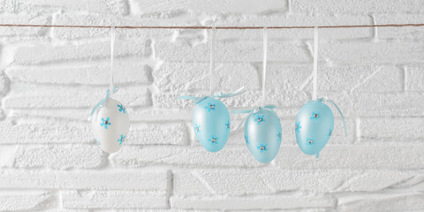 Blue Easter eggs hanging on a rope, white brick background. Banner