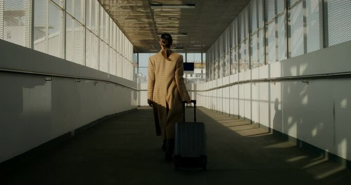 A woman in a coat with luggage in her hand walks through the railway station, she turns around looking at the camera