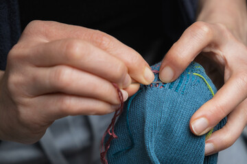 Mending clothes. Visible mending repairing sock. Darning old socks, reducing waste, slow fashion. Repair concept, selective focus. - obrazy, fototapety, plakaty