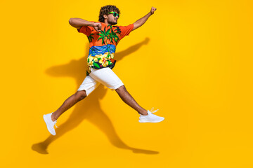 Fototapeta na wymiar Full length photo of positive guy wear hawaii shirt in glasses jumping look at promo run empty space isolated on yellow color background