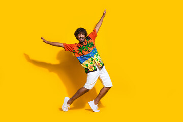 Fototapeta na wymiar Full size photo of ecstatic man dressed print shirt white shorts raising arms dancing on summer party isolated on yellow color background