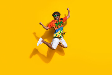Full length photo of ecstatic guy wear hawaii shirt sneakers in glasses jumping shout yes win...