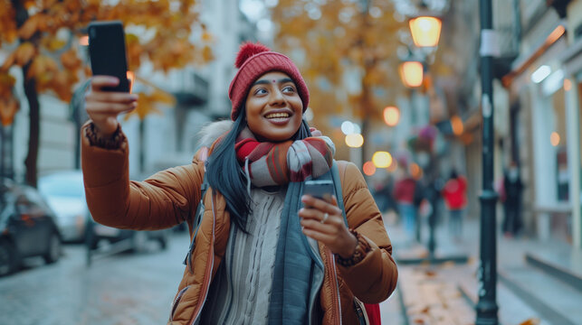 A walk through the city and a trip of an Indian young woman who stands on the street with a backpack and takes a selfie on the phone, talks with a smile on a video call, takes photos of landmarks